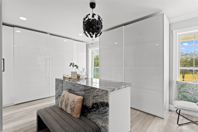 interior space with white cabinets, light hardwood / wood-style floors, hanging light fixtures, and light stone countertops