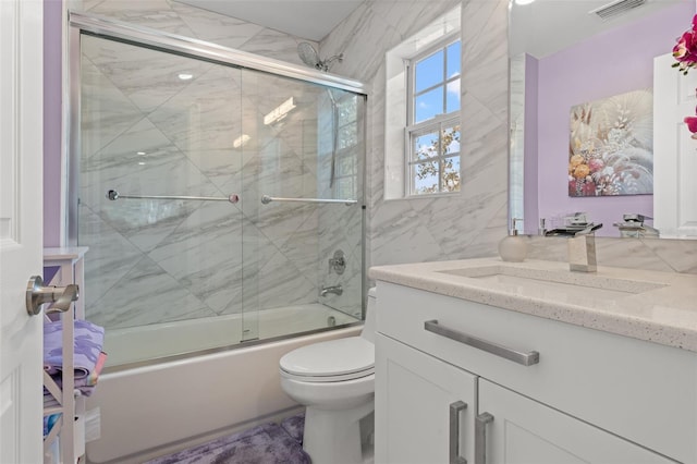 full bathroom with bath / shower combo with glass door, vanity, and toilet