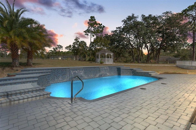 pool at dusk featuring a patio and a gazebo