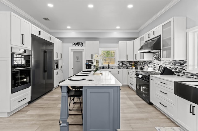 14485 Switch Back Rd, Brooksville, FL 34609 - kitchen with under cabinet range hood, black appliances, crown molding, a breakfast bar area, and a center island