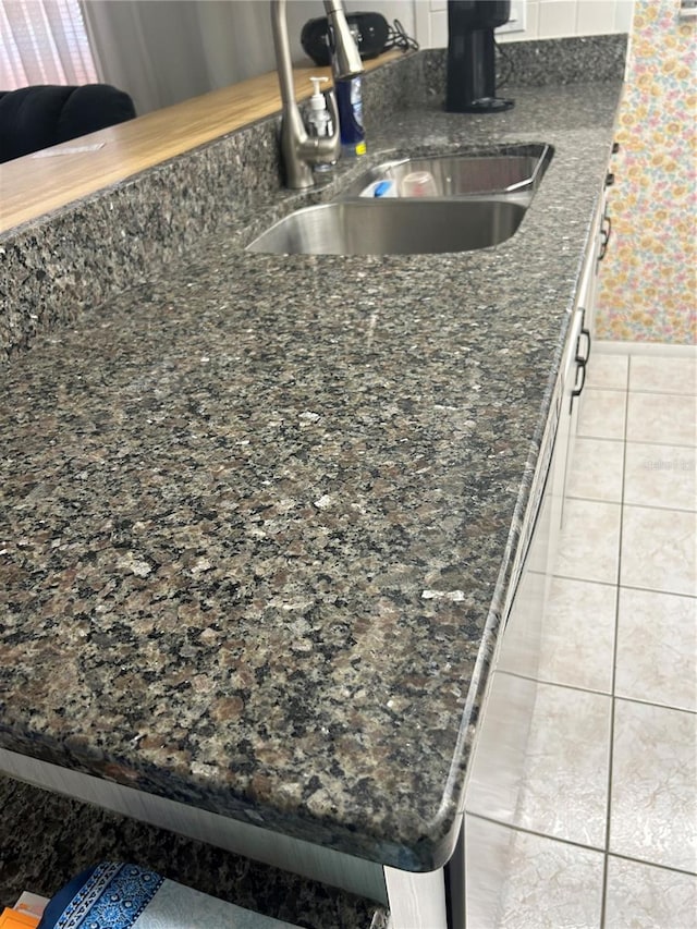 interior details featuring light tile patterned floors, dark stone countertops, white cabinets, and sink