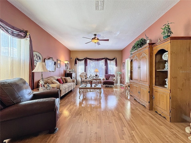 living room with ceiling fan, a textured ceiling, and light hardwood / wood-style floors