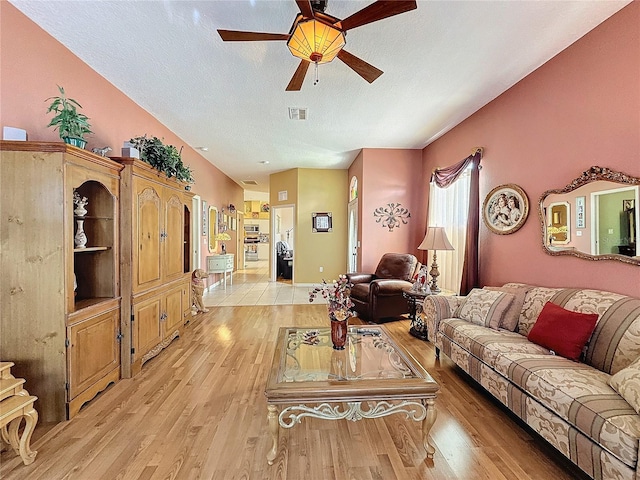 living room featuring ceiling fan, a textured ceiling, and light wood-type flooring