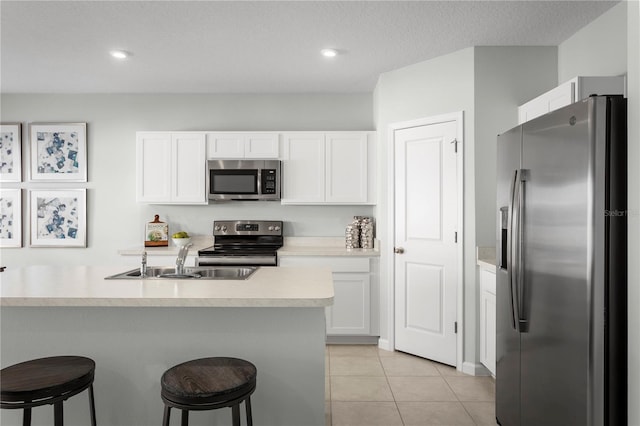 kitchen featuring stainless steel appliances, white cabinets, sink, light tile patterned floors, and a kitchen breakfast bar