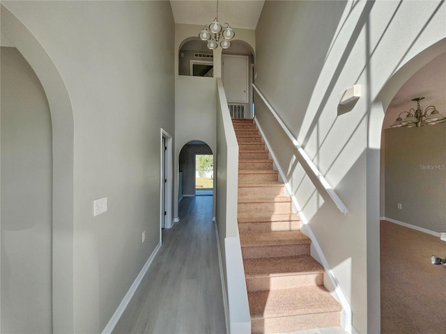 stairs with a towering ceiling, wood-type flooring, and a notable chandelier