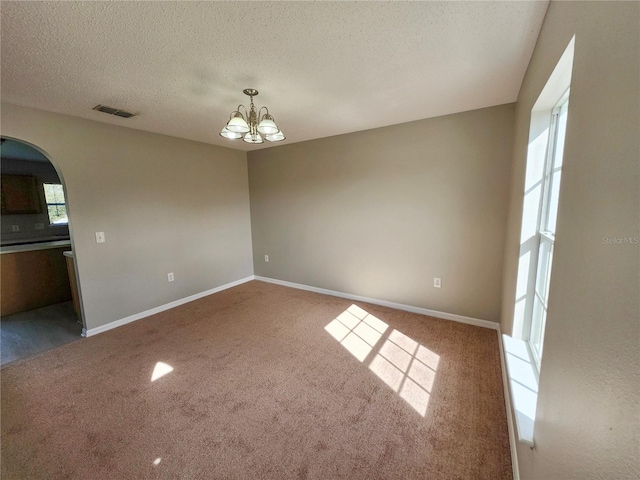 carpeted spare room featuring a textured ceiling and a chandelier