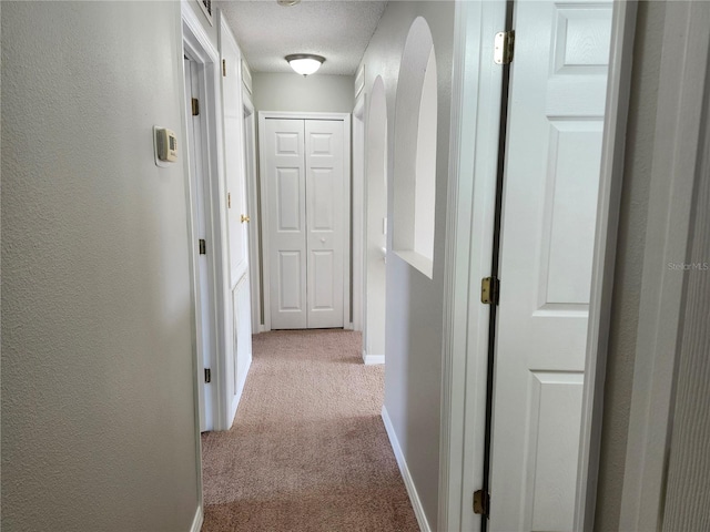 corridor with a textured ceiling and light carpet