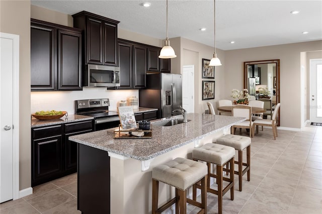 kitchen with a center island with sink, appliances with stainless steel finishes, a kitchen bar, hanging light fixtures, and sink