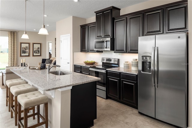 kitchen with stainless steel appliances, a center island with sink, sink, tasteful backsplash, and decorative light fixtures