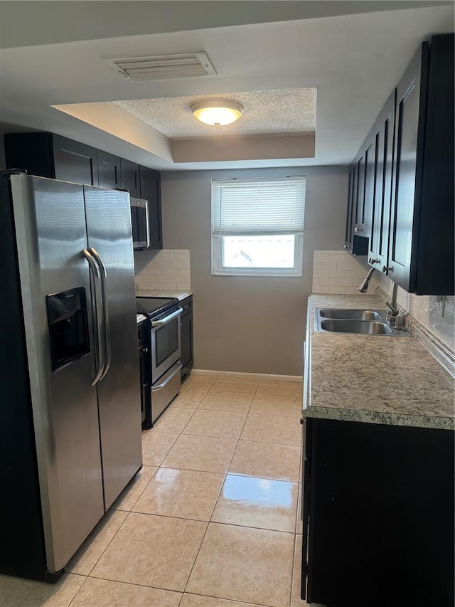 kitchen featuring stainless steel appliances, sink, light tile patterned floors, backsplash, and a tray ceiling