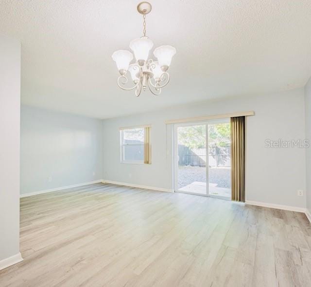 spare room featuring a chandelier, a textured ceiling, and light hardwood / wood-style flooring