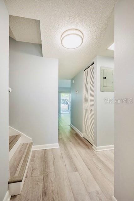 corridor with electric panel, a textured ceiling, and light wood-type flooring