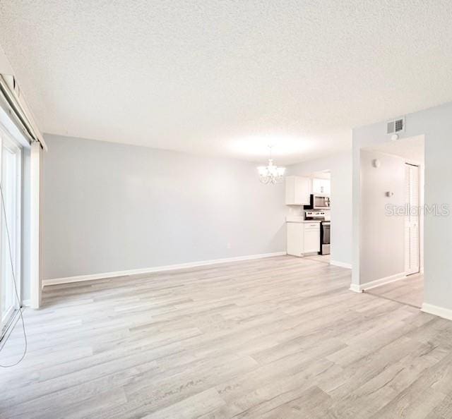 unfurnished living room featuring an inviting chandelier, light hardwood / wood-style floors, and a textured ceiling