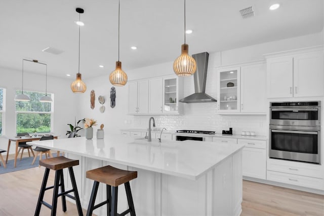 kitchen with pendant lighting, wall chimney exhaust hood, white cabinets, and stainless steel appliances