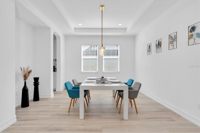 dining area with a tray ceiling and light hardwood / wood-style flooring