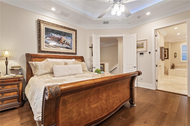 bedroom featuring dark hardwood / wood-style floors, connected bathroom, ceiling fan, and a tray ceiling