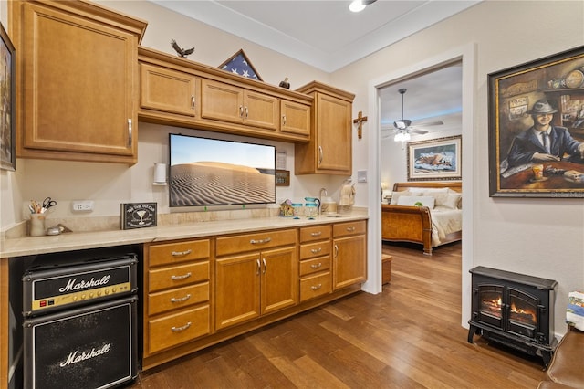 kitchen with crown molding, ceiling fan, dark hardwood / wood-style flooring, and a wood stove