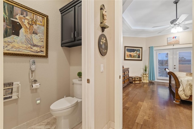 bathroom with hardwood / wood-style floors, ceiling fan, toilet, a raised ceiling, and french doors