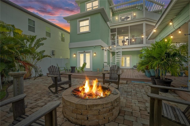 patio terrace at dusk with a fire pit, french doors, a balcony, and a deck