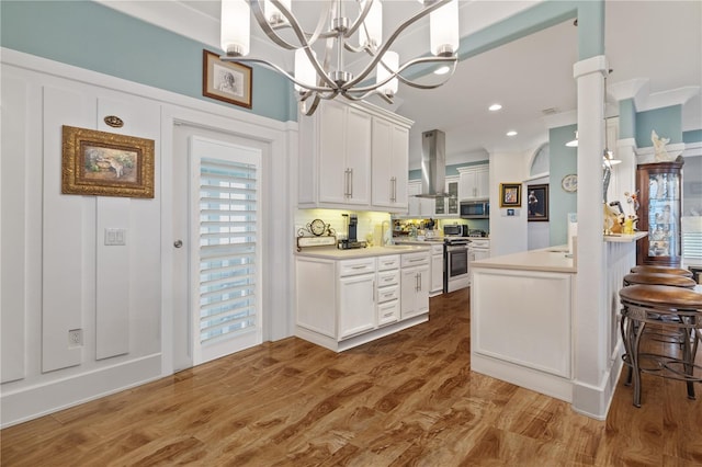 kitchen with appliances with stainless steel finishes, pendant lighting, island range hood, white cabinetry, and a kitchen bar