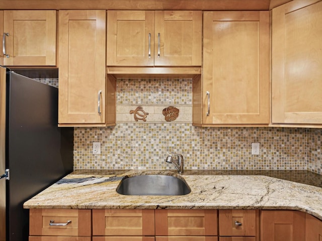 kitchen featuring light stone countertops, stainless steel fridge, sink, and backsplash