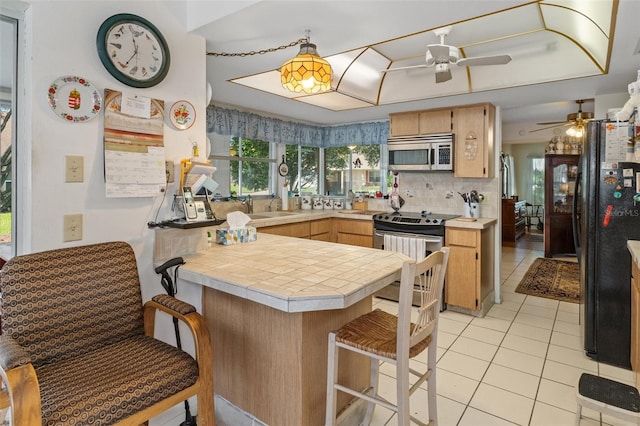 kitchen featuring sink, kitchen peninsula, appliances with stainless steel finishes, tasteful backsplash, and tile counters