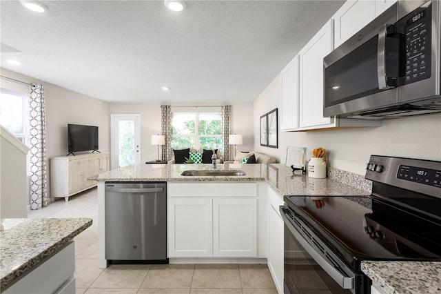 kitchen featuring white cabinetry, sink, kitchen peninsula, light stone counters, and appliances with stainless steel finishes