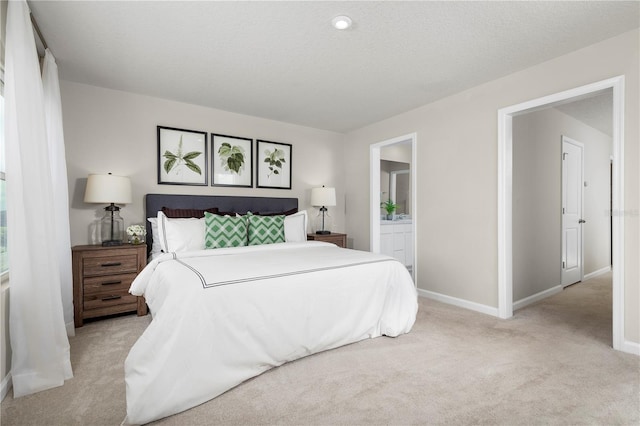 bedroom with ensuite bathroom, light colored carpet, and a textured ceiling