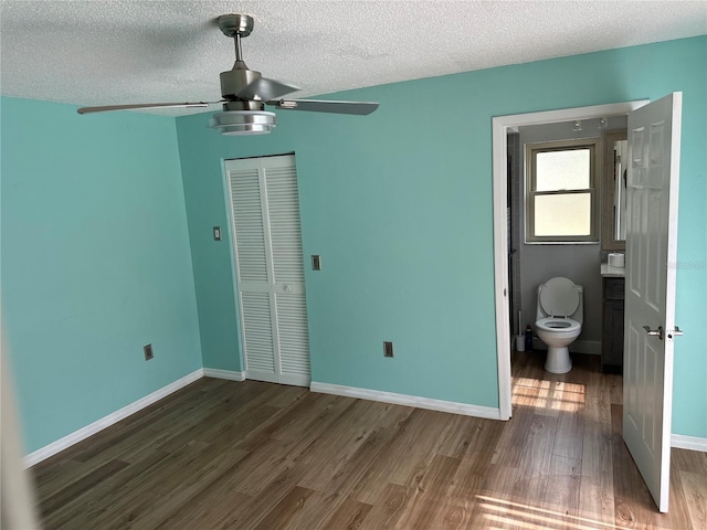 unfurnished bedroom featuring ensuite bathroom, ceiling fan, dark hardwood / wood-style floors, a textured ceiling, and a closet