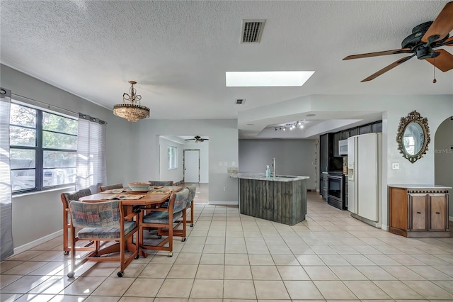 dining area featuring light tile patterned flooring, a skylight, sink, and ceiling fan