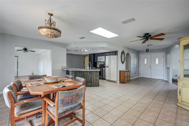 tiled dining area featuring ceiling fan with notable chandelier, a textured ceiling, and a skylight