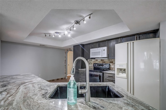 kitchen featuring light stone counters, decorative backsplash, sink, a tray ceiling, and white appliances