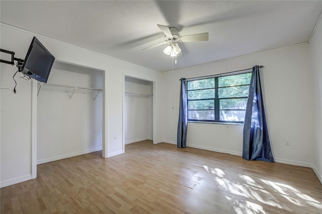 unfurnished bedroom featuring light wood-type flooring, ceiling fan, a textured ceiling, and multiple closets