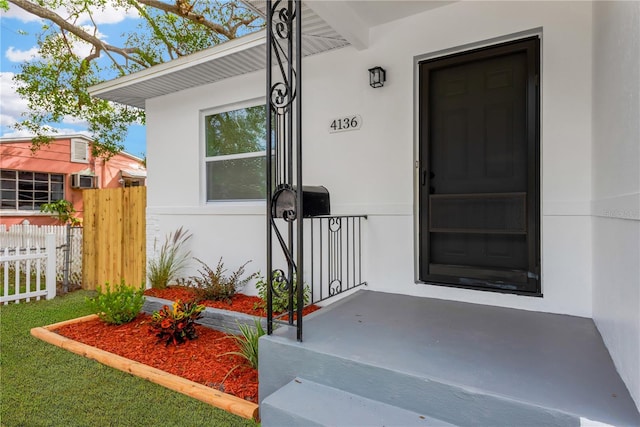 view of exterior entry with fence and stucco siding