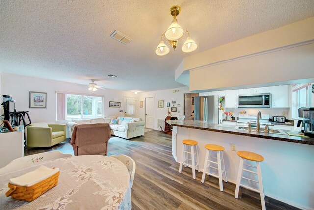 dining area with a textured ceiling, sink, wood-type flooring, and ceiling fan with notable chandelier