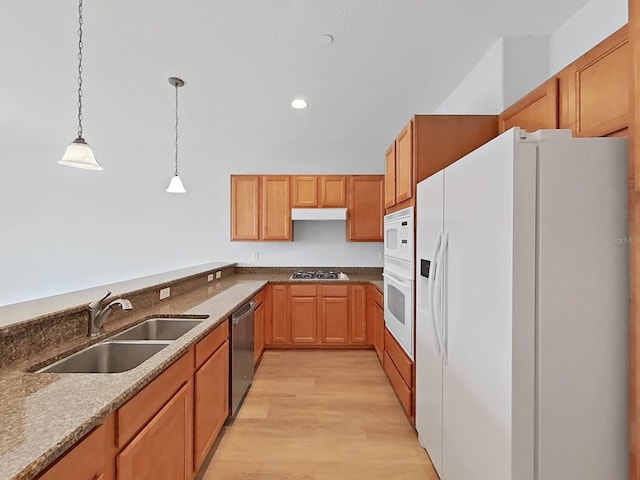 kitchen featuring stainless steel appliances, light wood-type flooring, decorative light fixtures, stone countertops, and sink