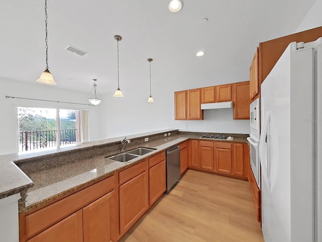 kitchen with stone countertops, sink, appliances with stainless steel finishes, decorative light fixtures, and light hardwood / wood-style flooring