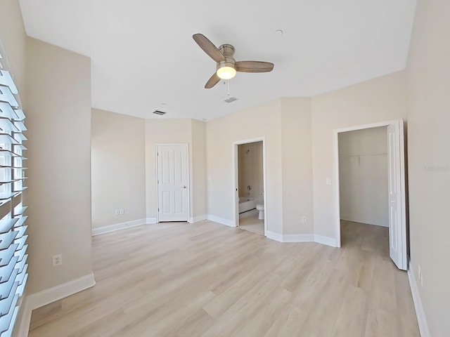 unfurnished bedroom with connected bathroom, ceiling fan, a closet, light wood-type flooring, and a spacious closet