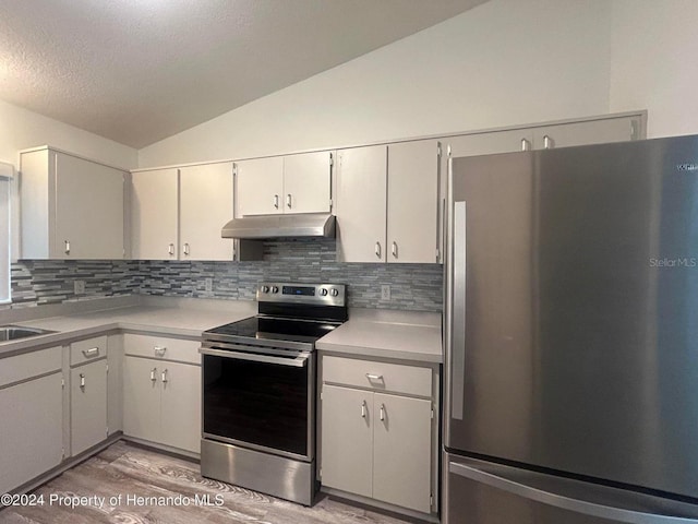 kitchen featuring stainless steel appliances, light hardwood / wood-style floors, tasteful backsplash, white cabinets, and vaulted ceiling