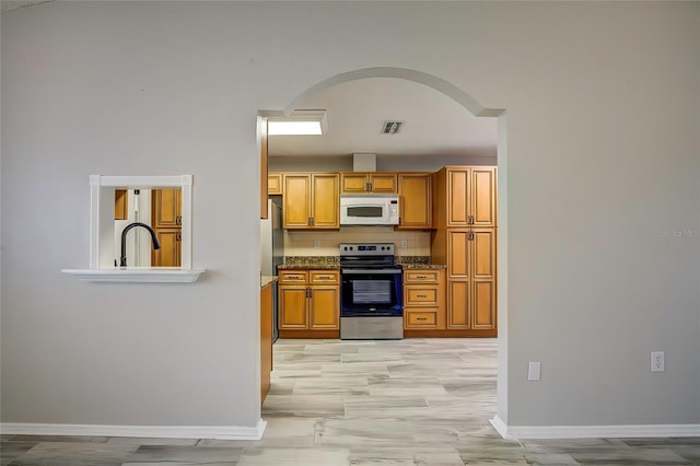 kitchen with dark stone counters, tasteful backsplash, appliances with stainless steel finishes, and light hardwood / wood-style floors