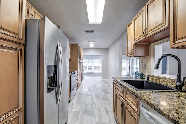 7499 Heather Walk, Weeki Wachee, FL 34613 - kitchen with stainless steel appliances, a sink, a textured ceiling, dark stone counters, and baseboards