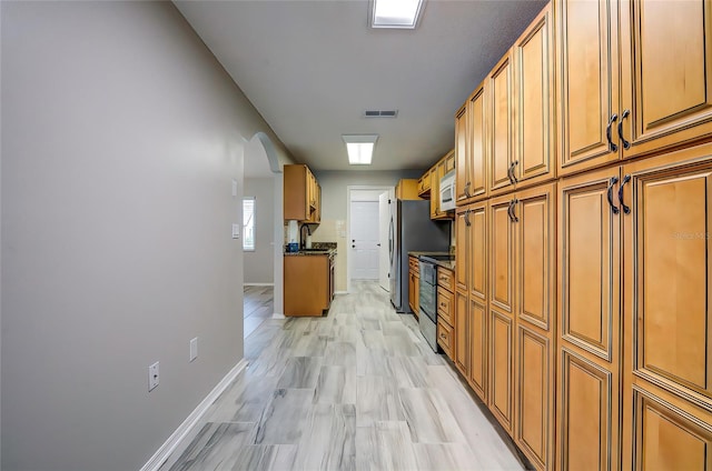 kitchen featuring dark stone counters, appliances with stainless steel finishes, sink, and light hardwood / wood-style flooring