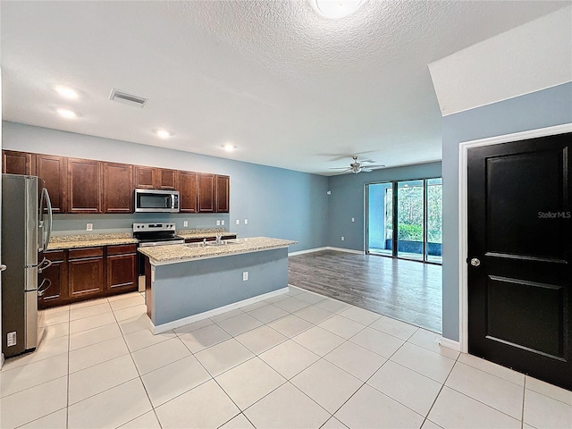 kitchen with ceiling fan, light hardwood / wood-style floors, a textured ceiling, a center island with sink, and appliances with stainless steel finishes