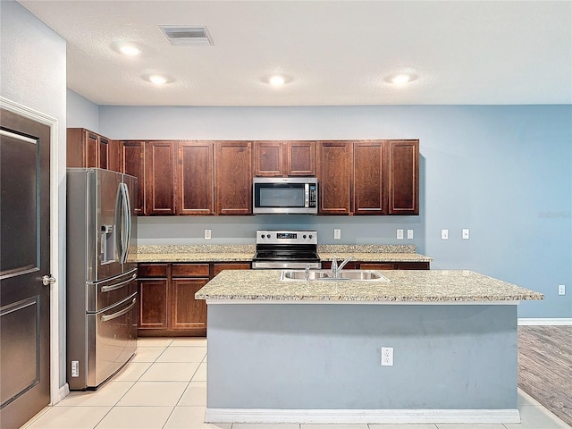 kitchen featuring sink, stainless steel appliances, light stone counters, and an island with sink