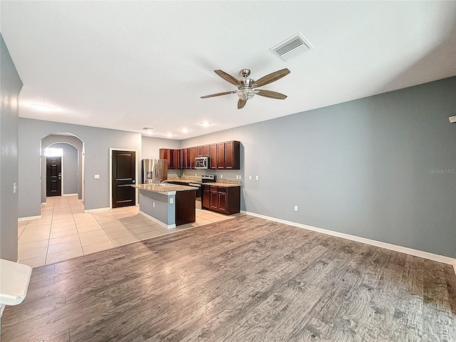 kitchen with ceiling fan, light hardwood / wood-style flooring, a kitchen island with sink, a breakfast bar, and appliances with stainless steel finishes