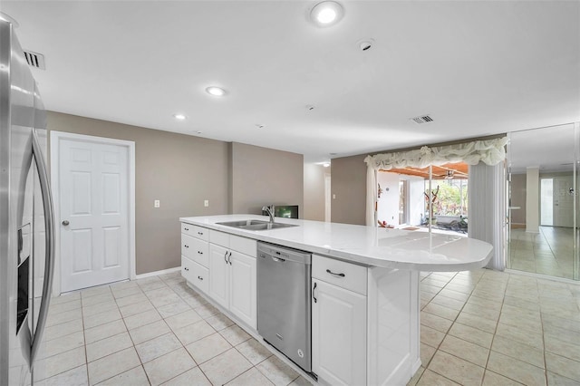 kitchen with stainless steel appliances, white cabinetry, light tile patterned floors, sink, and a kitchen island with sink