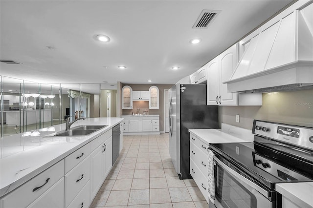 kitchen featuring sink, custom exhaust hood, light tile patterned floors, white cabinetry, and appliances with stainless steel finishes