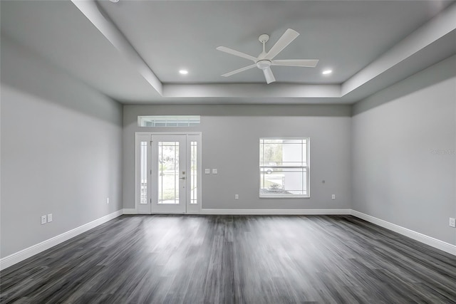 empty room featuring a raised ceiling, ceiling fan, dark hardwood / wood-style flooring, and plenty of natural light