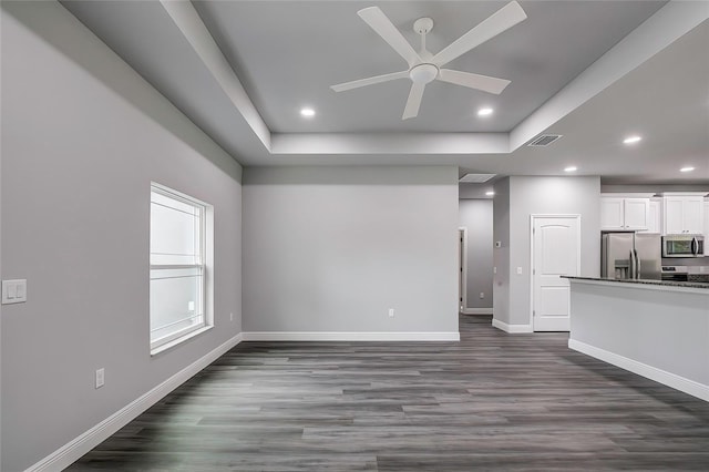 unfurnished living room featuring ceiling fan, dark wood-type flooring, and a tray ceiling