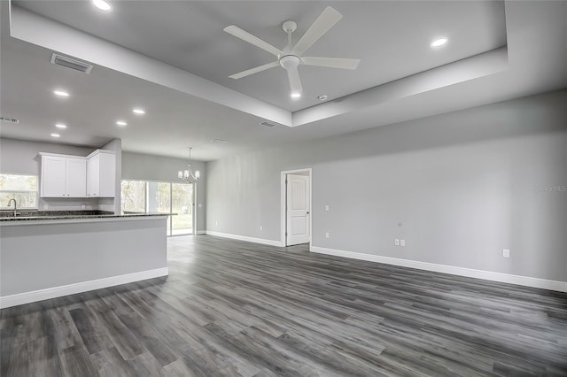 unfurnished living room featuring a tray ceiling, dark hardwood / wood-style flooring, ceiling fan with notable chandelier, and sink